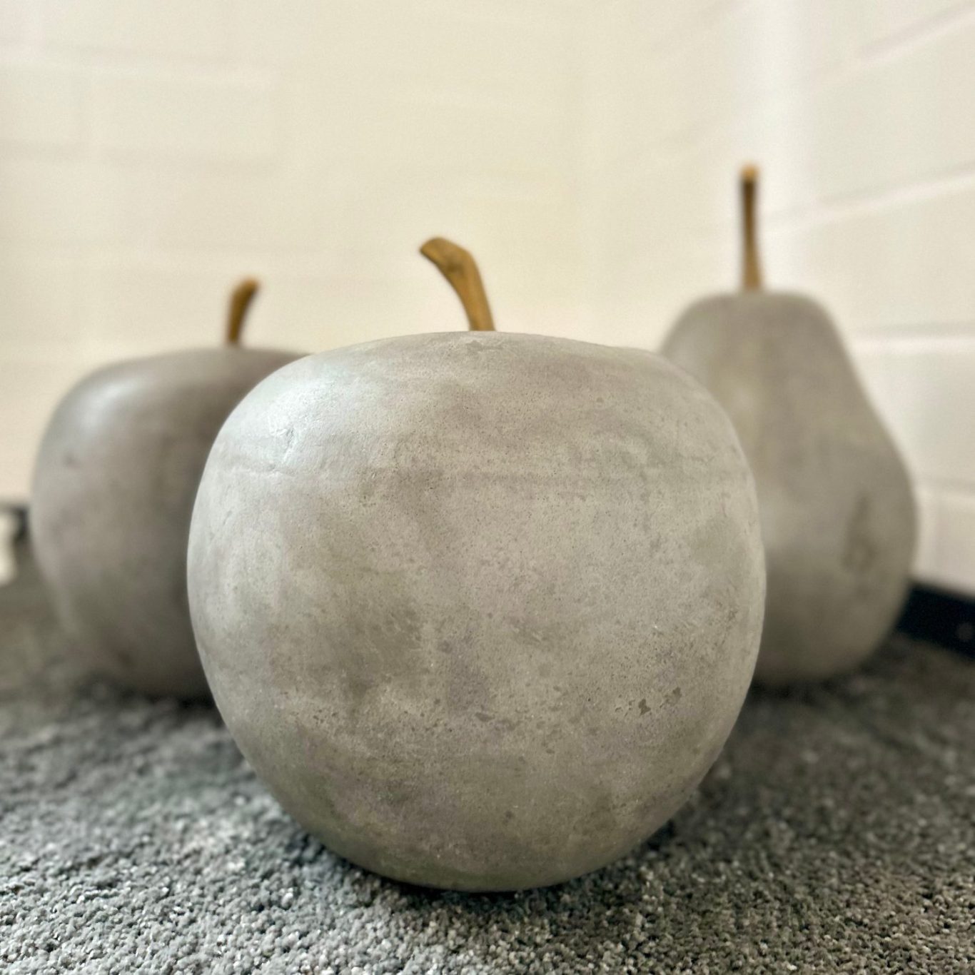 Wohnraum Deko Drei graue Betonbirnen mit braunen Stielen auf einem hellen Untergrund.
