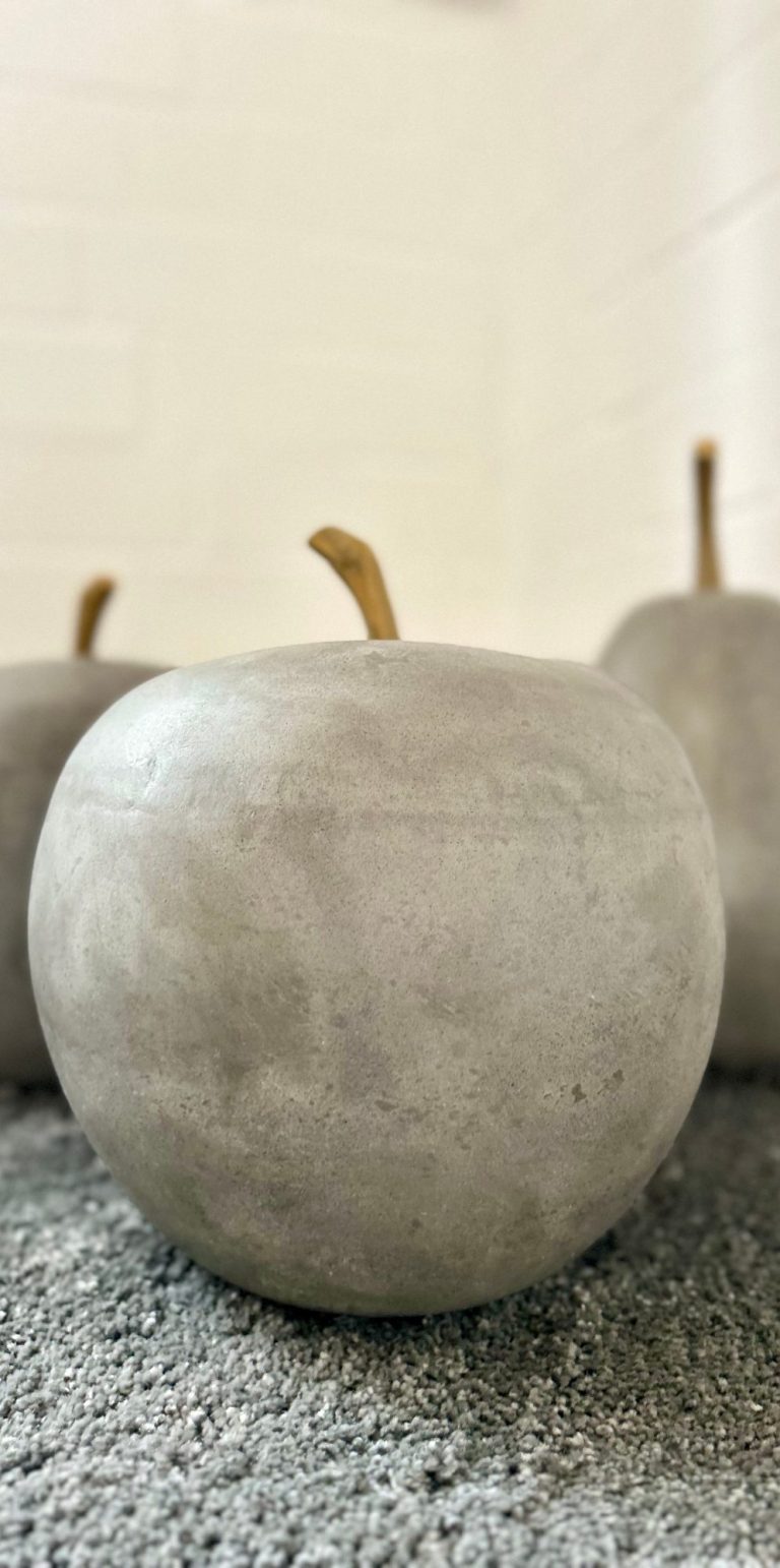 Grau lackierte Äpfel aus Beton auf einem neutralen Hintergrund.