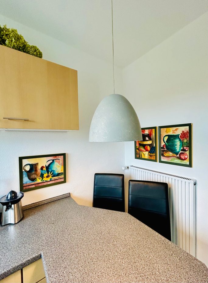 Moderne Küche mit einem runden Lampenschirm, zwei Stühlen und bunten Wandbildern.