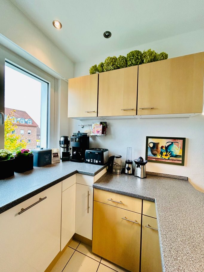 Moderne Küche mit hellem Holzschrank, Kaffeeautomat und Pflanzen auf der Fensterbank.