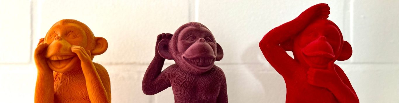 Drei bunte Affenskulpturen in verschiedenen Farben, die unterschiedliche Gesten zeigen.