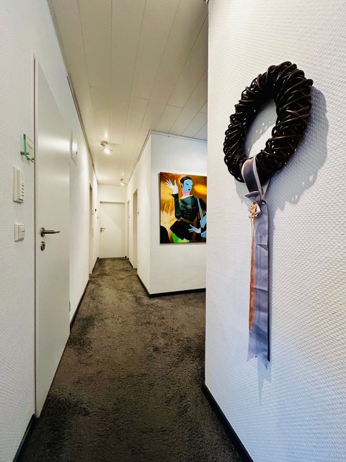 Langer Flur mit einer Wanddekoration in Form eines Kranzes und einem Gemälde.