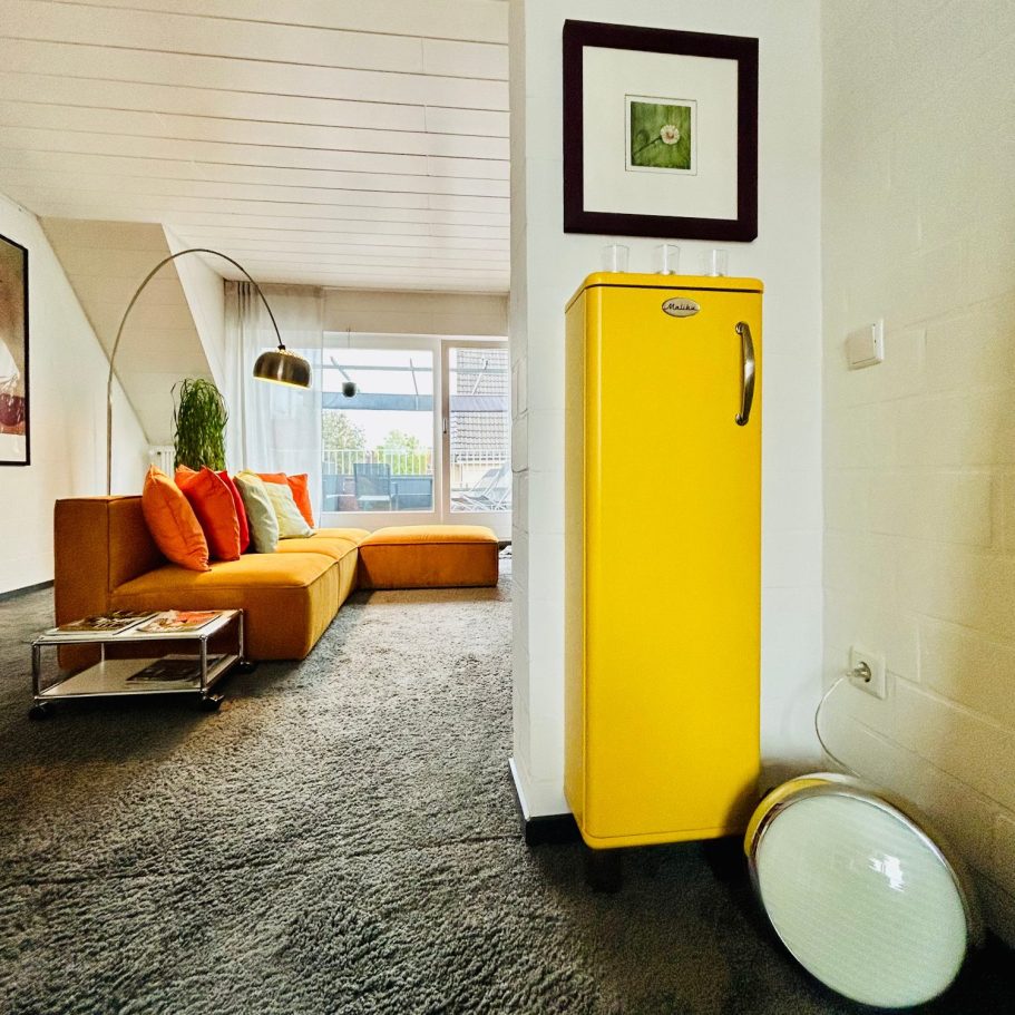 Gelber Malibu Schrank in modernem Wohnzimmer mit orangefarbenem Sofa und Pflanzen.