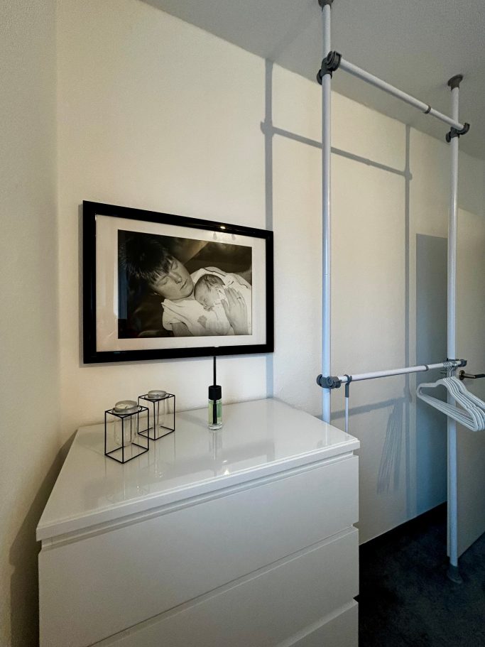 Moderne Garderobe mit weißem Schrank, Bild an der Wand und minimalistischen Accessoires.