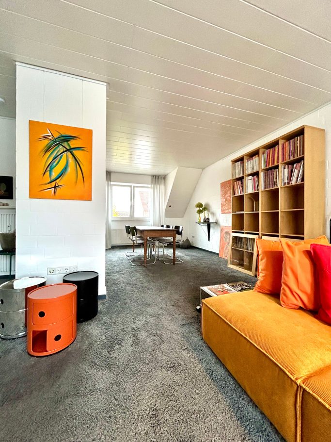 Heller Wohnraum mit orangefarbenem Sofa, Bücherschrank und Tisch.