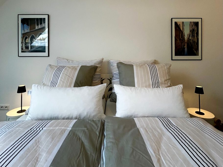 Doppelbett mit gestreiften Bettwäsche, zwei Nachttischen und Bildern an der Wand.