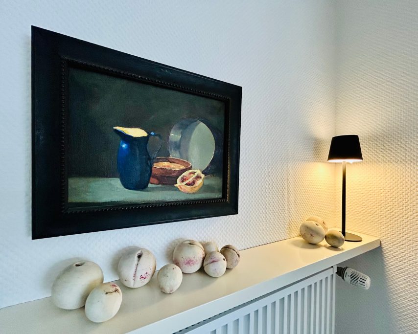 Stillleben mit blauer Kanne, Brot und dekorativen Objekten auf einem Regal.